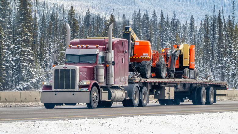 A flatbed smi trailer carrying a huge load of construction equipment