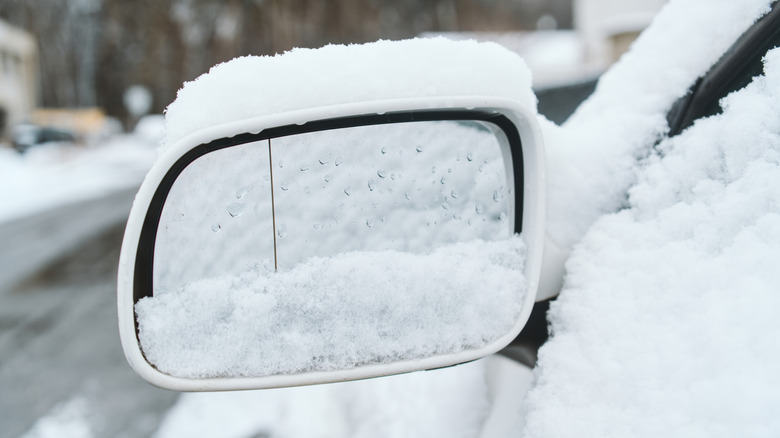 Snow-covered side mirror of a car with water droplets