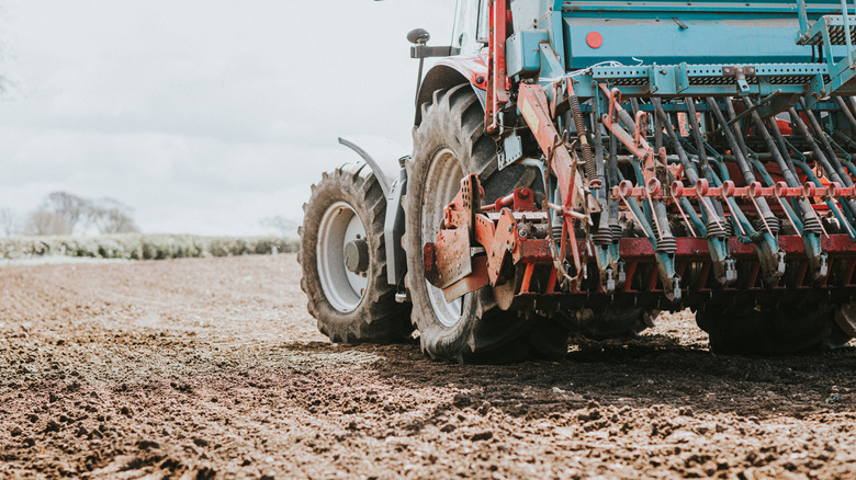 A shiny red tractor drives in a ploughed field