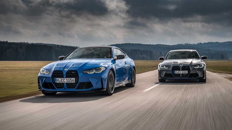 2022 BMW M3 and M4 Competition driving side-by-side down road, front-view