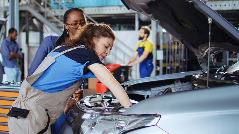 Two mechanics in a shop working in a car's engine bay