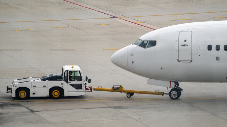 A pushback tug connected to the front landing gear of a Boeing 737 with a long yellow tow hook