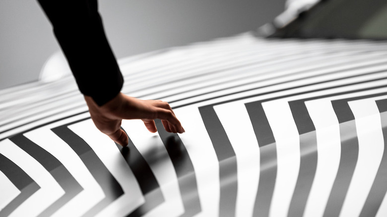 A hand traces the zig-zag pattern of black-and-white lines on the hood of a car