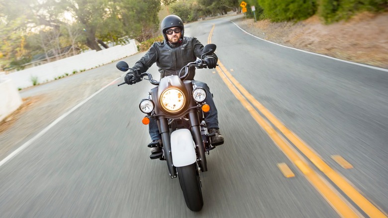 A motorcyclist riding close to the yellow centerline on a rural roadway.