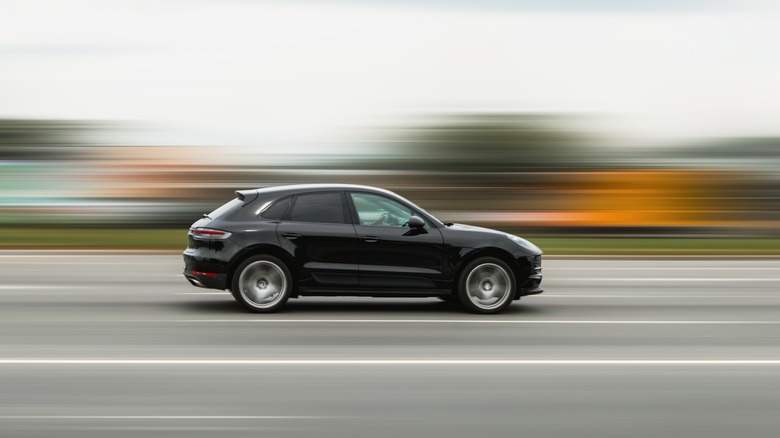 The side profile of a black Porsche Macan on the move, showing the wheels in motion
