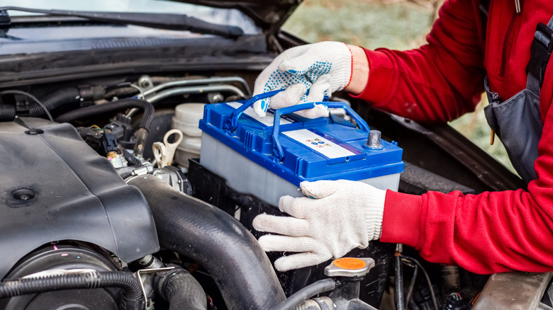 A car mechanic installs a battery in a car