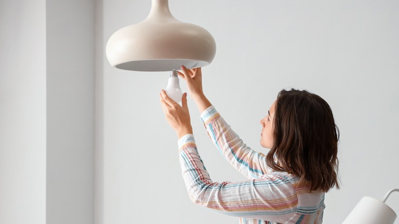 A woman changing the LED bulb in a hanging light.