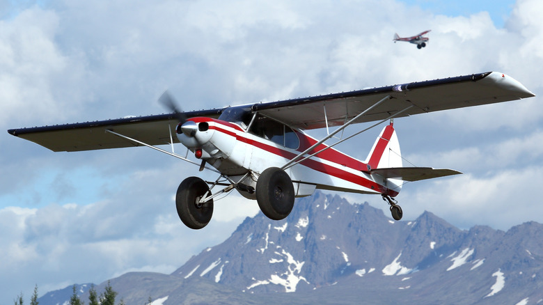 A Super Cub bush plane taking off with mountains in the background