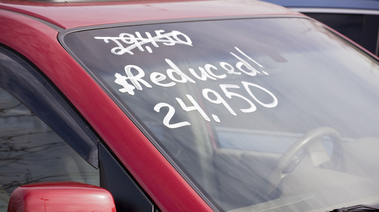 A handwritten sign in white marker pen on the windscreen of a red vehicle announces a reduced price
