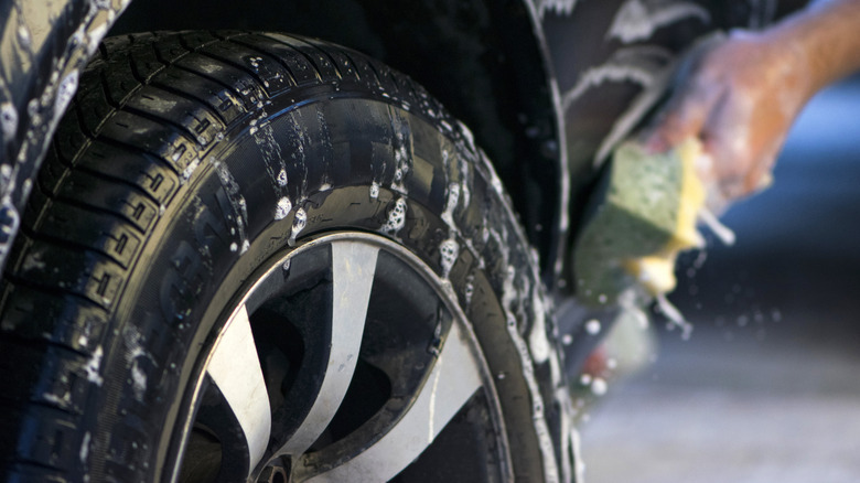 A close-up image of a man washing a tire with a sponge