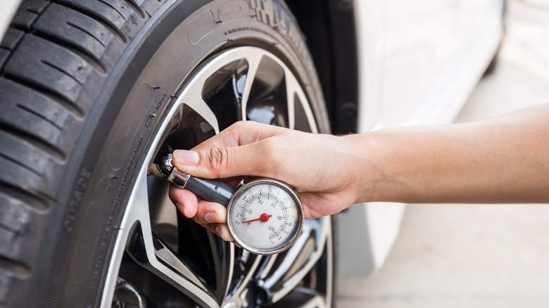 A hand holds a gauge while measuring tire pressure.