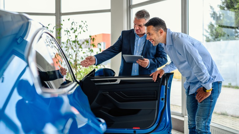A salesman shows a potential customer the inside of a blue car at a dealership.