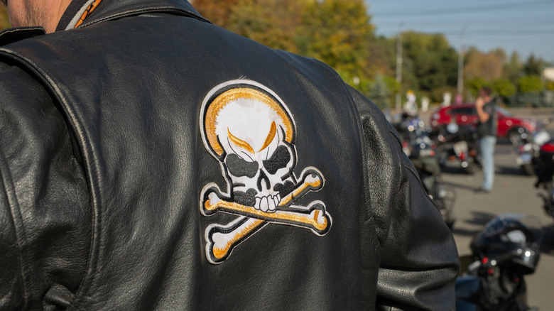 A biker wearing a black leather jacket with a skull on the back
