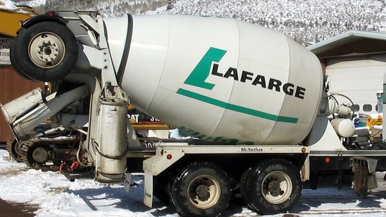 A Lafarge cement truck whose rear holds a raised tag axle, which is a bar that holds two wheels, with tires attached.