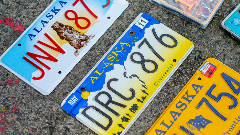 Three Alaska license plates showing different designs on a concrete surface, on display at an outdoor sale.