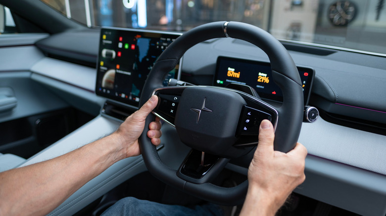 A Polestar 4 steering wheel being held by a man's hands.