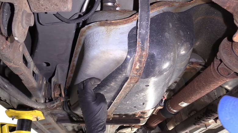 A person inspecting the fuel lines and fuel tank underneath their car.