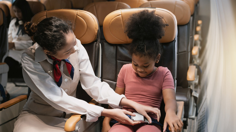 Air hostess fastening a female child passenger's safety belt before takeoff