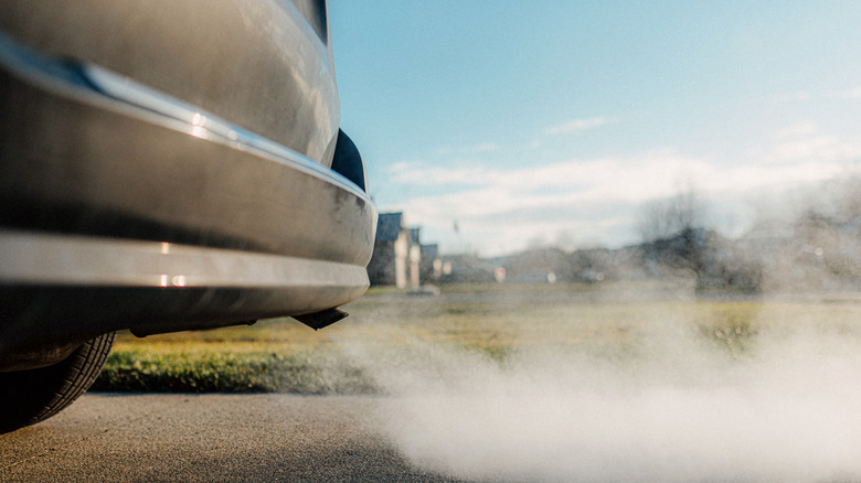 A car emits exhaust fumes from its tailpipe as it drives down a suburban road