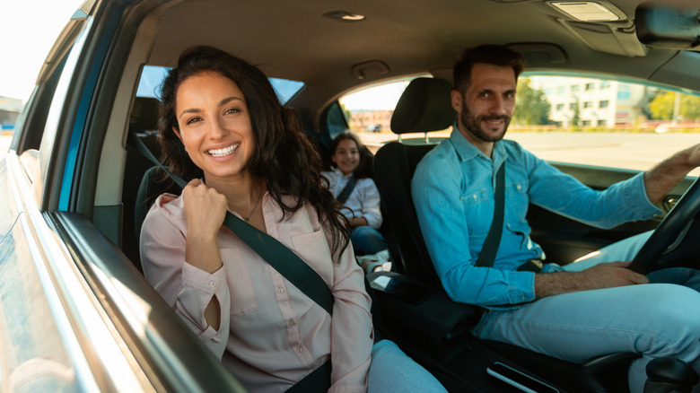 Happy family enjoying a drive together, woman sitting in front passenger's seat and smiling at camera.