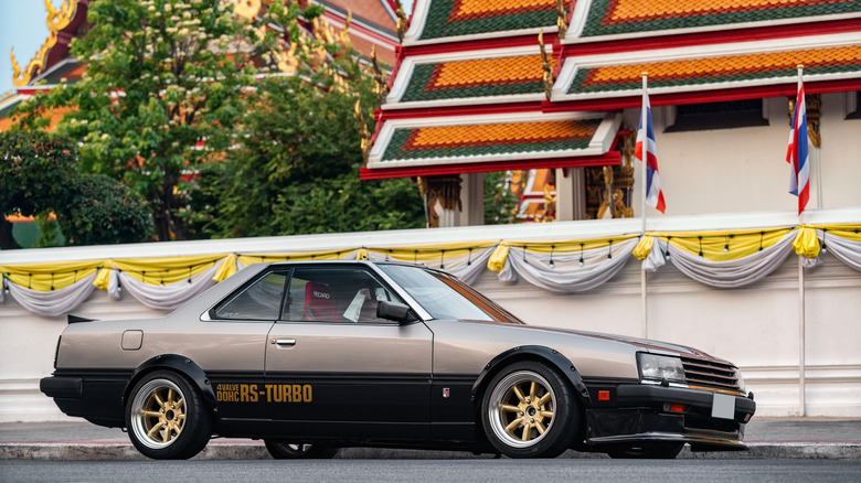 A tuned Nissan Skyline R30 with Watanabe wheels parked outside a temple