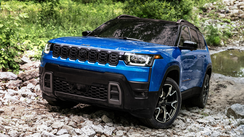 Front quarter view of a modern-looking blue Jeep in a rocky waterway.