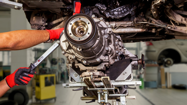 Mechanic working on a transmission on a car lift in a workshop.