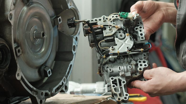 A mechanic working on a torque converter next to a transmission.