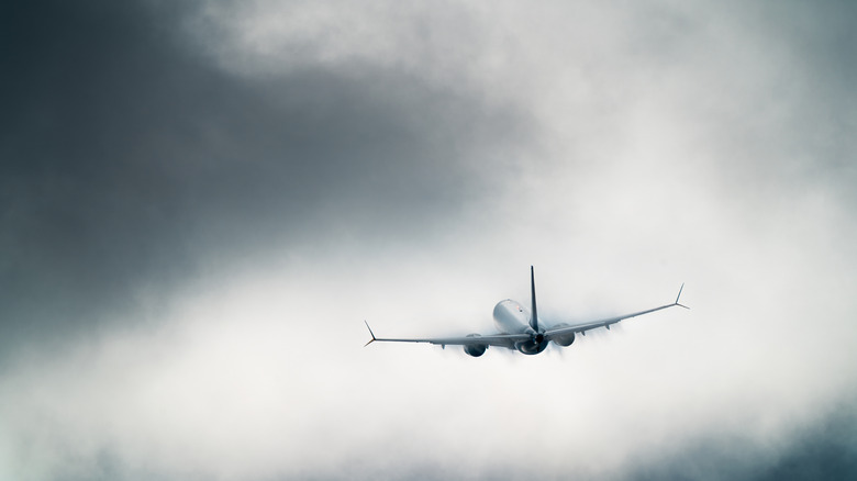 A commercial airplane is captured from the rear as it enters dense clouds shortly after takeoff.