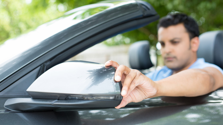 A man adjusting the side mirror of his car