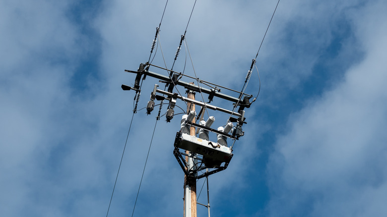 The top of a utility pole against a cloudy blue sky.