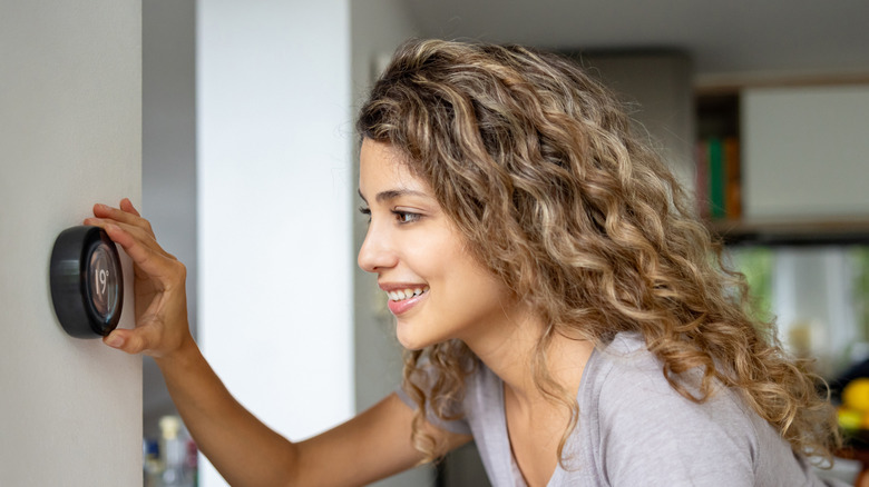 A smiling woman adjusting a smart thermostat