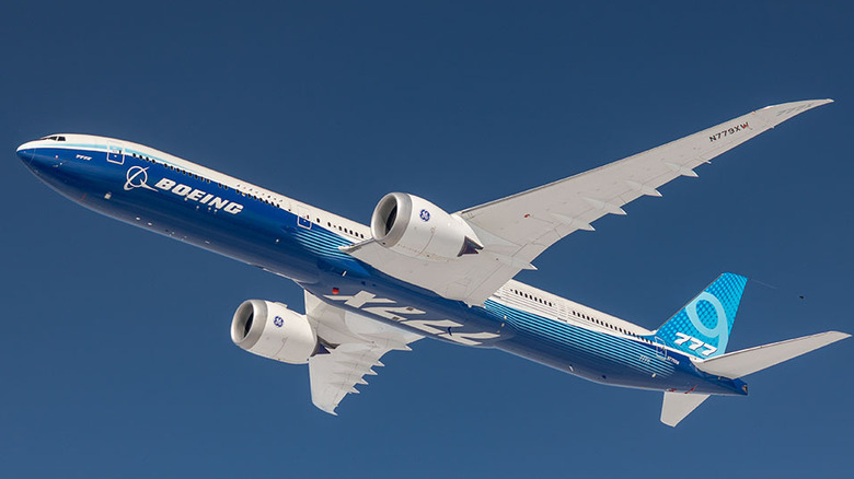 A Boeing 777X in the air with a bright blue sky