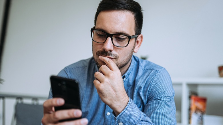 Young thoughtful man looking at mobile phone