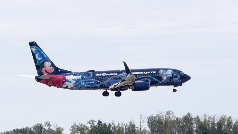 A Westjet passenger plane with a Disney livery flying at a very low altitude, side view