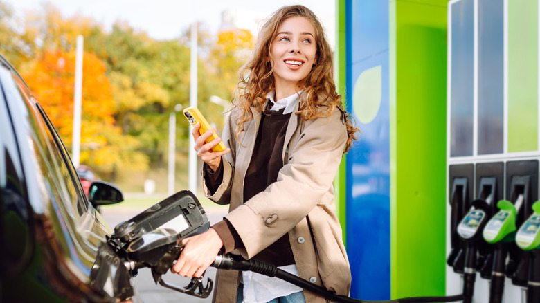 A smiling blonde woman pumping gas into her vehicle at brightly-colored gas station
