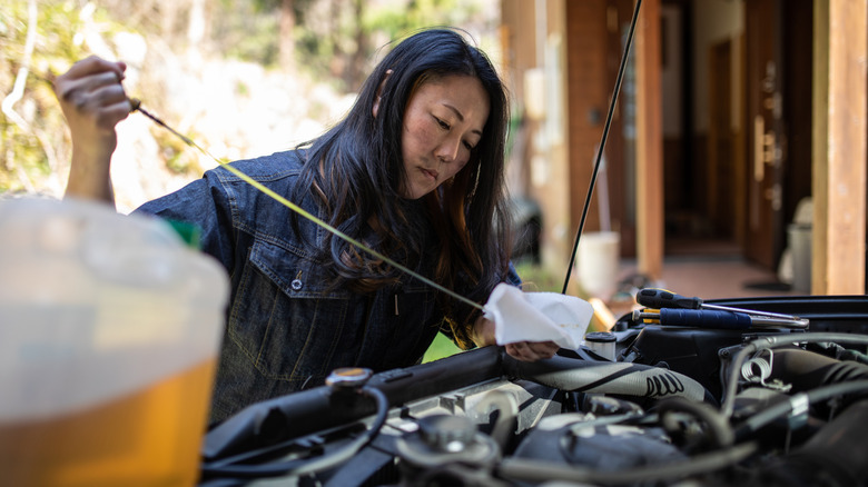 A woman getting dirty while working under the hood of a car.