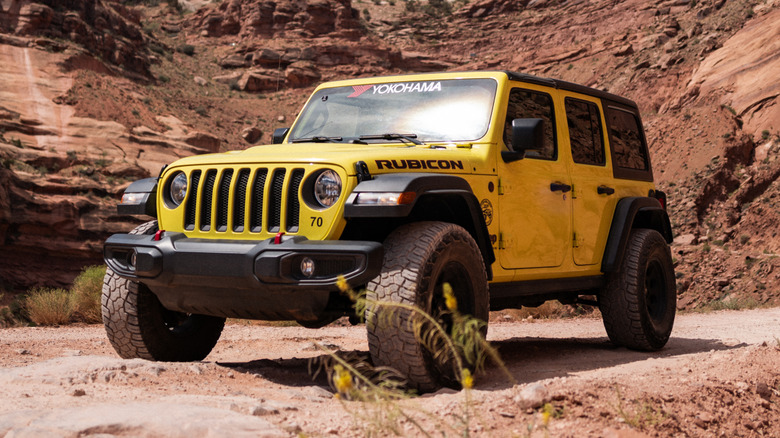 A yellow off-road-ready Jeep Wrangler Rubicon driving through rocky terrain.