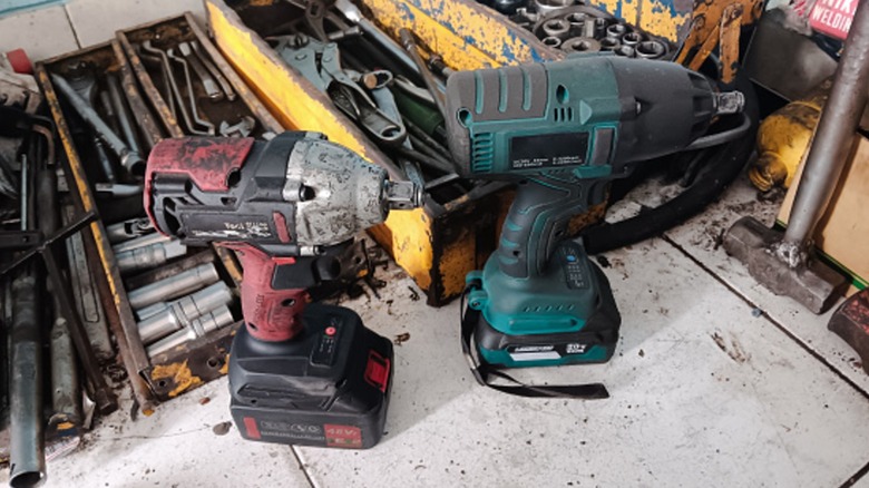 Used cordless power tools on a table with other assorted hand tools.