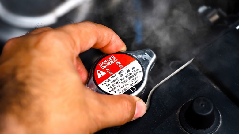 a person removing the radiator cap from a hot engine