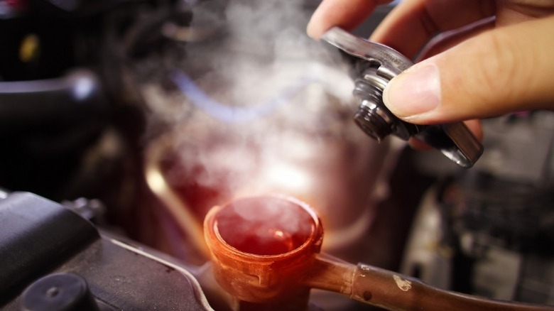 a person removing the radiator cap from an overheating engine