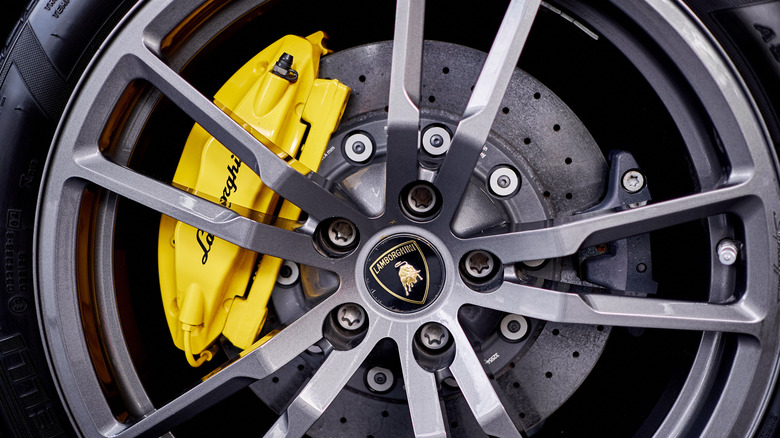 A close-up of a Lamborghini wheel with titanium lug nuts in front of a yellow brake calliper.