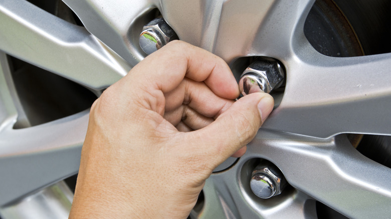 A close-up of a person tightening wheel lug nuts by hand on a car.