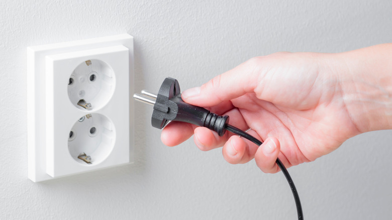 A womans hand equipping a power cord into a socket