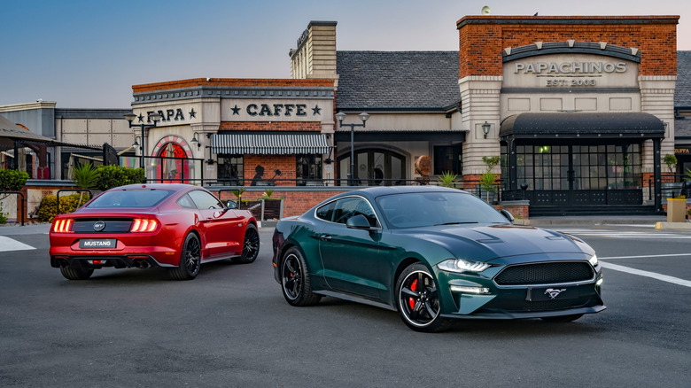 Ford Mustang Bullitt, front-right view, and Ford Mustang GT, rear-right view, in parking lot with restaurant in background