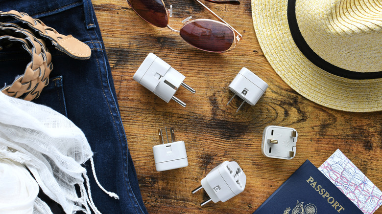 Various adapters and converters alongside a passport and other travel gear