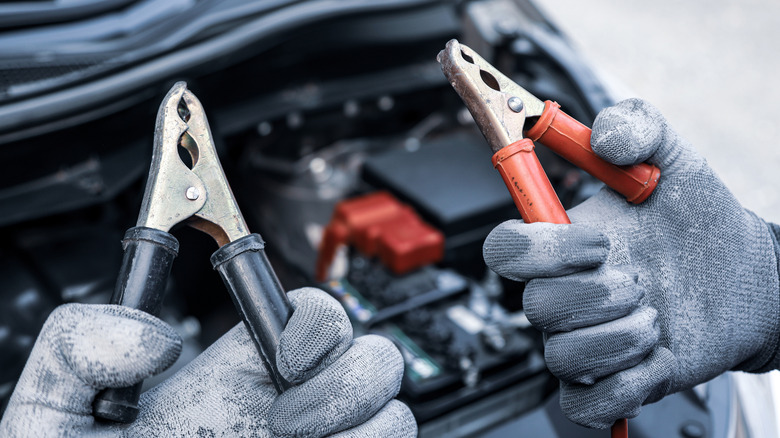 A person holding jumper cables beside a car battery.