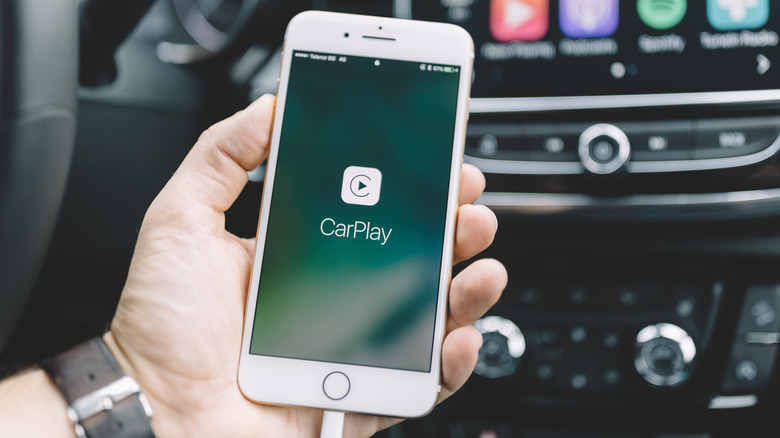 Person selecting maps icon on CarPlay infotainment screen with left index finger