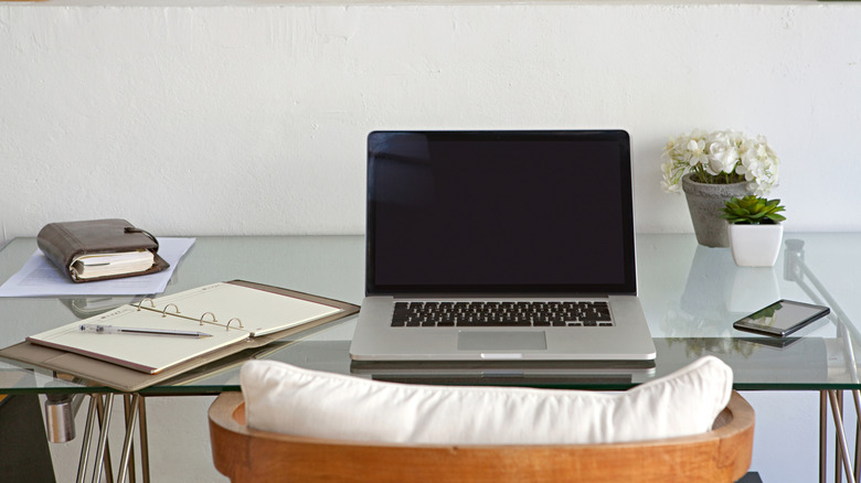 A desk with a laptop, smartphone and planners resting on it.