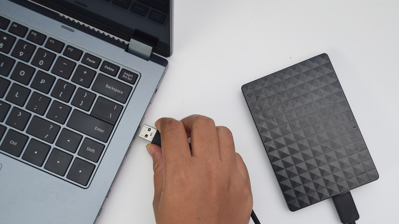 Person plugging external hard drive into laptop.